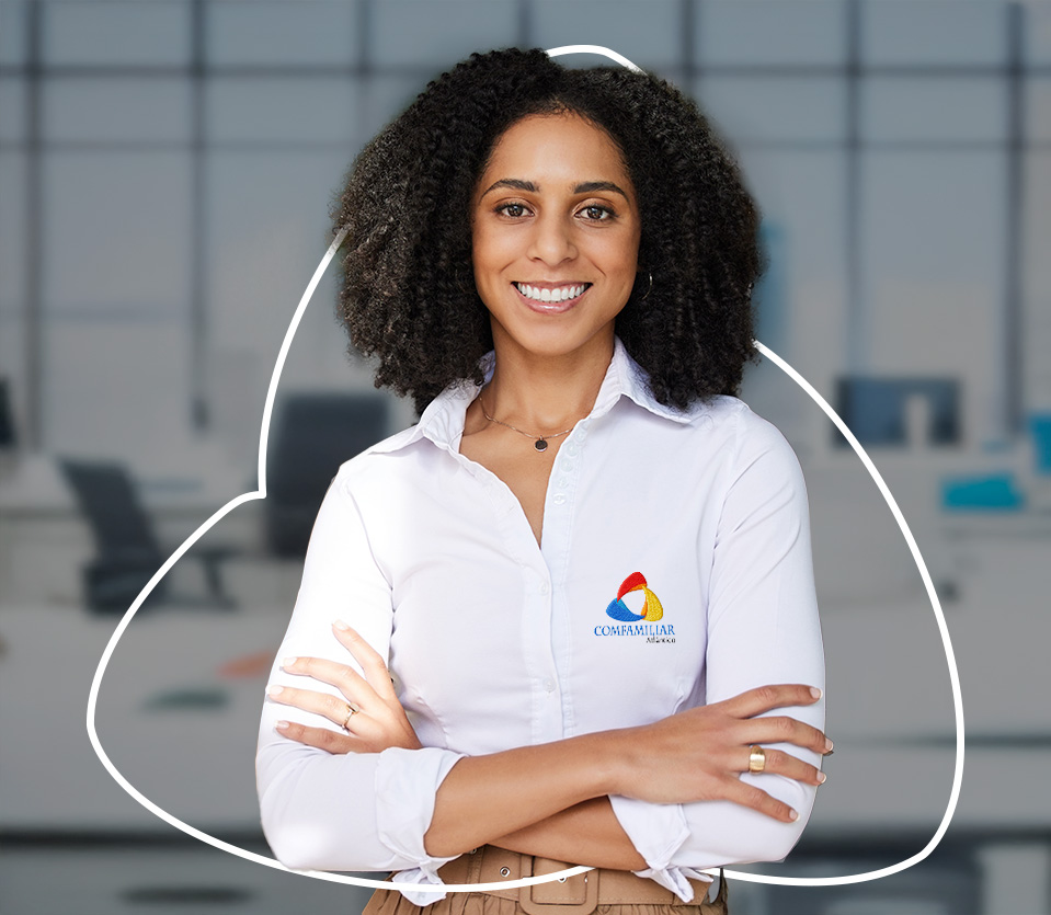 Mujer de piel clara con cabello rizado, sonriente, vestida con camisa blanca y pantalones beige, de pie en un entorno de oficina con mobiliario moderno y fondo difuso.