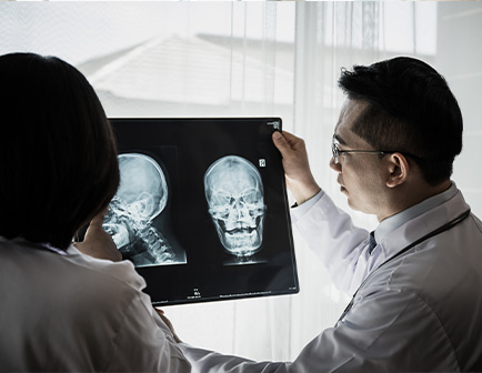 Médico sostiene radiografías del cráneo mientras explica a un colega en un entorno clínico iluminado.