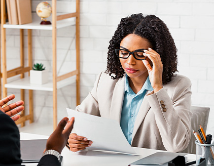 Mujer con gafas revisando documentos en una mesa, con fondo de estantería y decoración minimalista.
