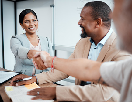 Dos personas se dan la mano en una reunión, con una mujer sonriendo y un hombre de pie, en un entorno de oficina.