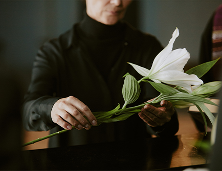 Persona sosteniendo un lirio blanco, con fondo oscuro y ambiente acogedor.