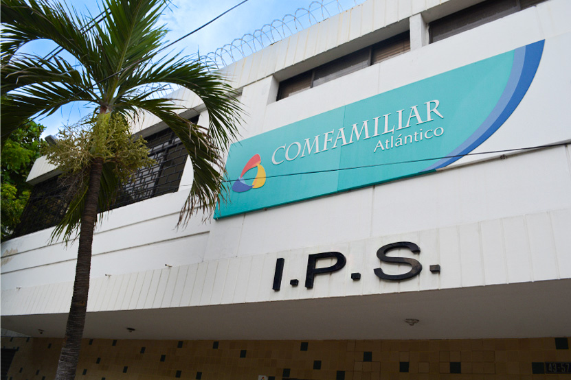 Fachada de un edificio con el letrero "COMFAMILIAR Atlántico" y las letras "I.P.S." en la parte inferior. Se observan plantas y un cielo despejado.