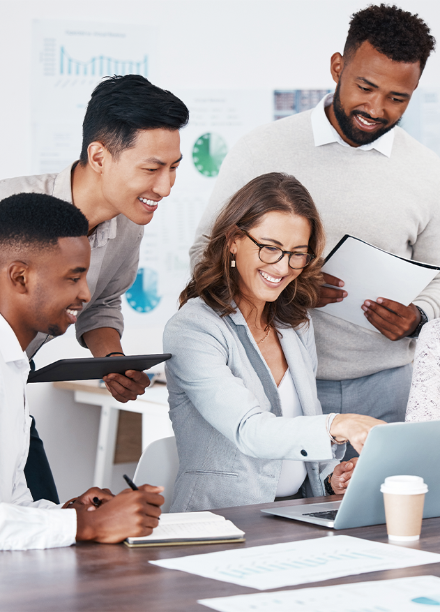 Grupo de cuatro personas colaborando en una mesa, observando una computadora portátil. Dos hombres y dos mujeres, con documentos y tabletas, en un entorno de oficina moderno.