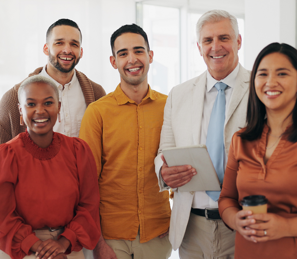 Grupo de cinco personas sonriendo, con diferentes atuendos en tonos cálidos. Se encuentran en un entorno luminoso y moderno, sosteniendo una tableta y una taza de café.