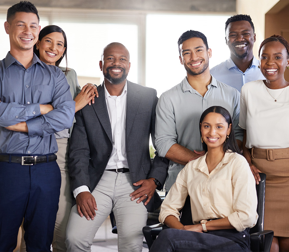 Grupo de ocho personas sonriendo, en un entorno de oficina con luz natural, vestimenta formal y casual.