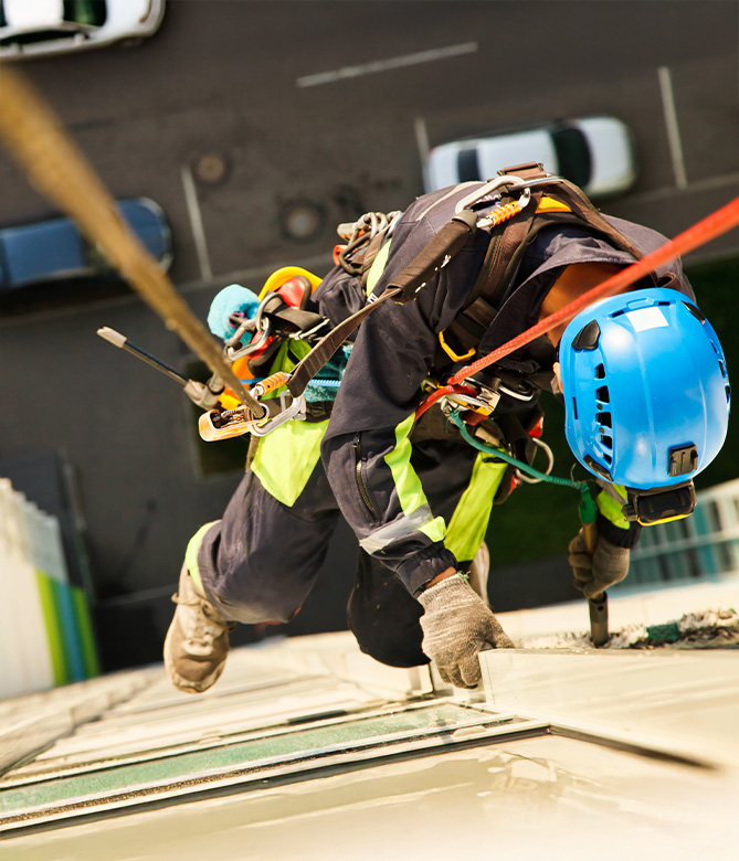 Trabajadores en altura descendiendo por un edificio con cuerdas, usando cascos azules y ropa de seguridad.
