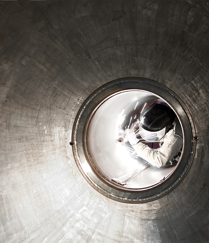 Astronauta reflejado en un visor circular, rodeado de superficies metálicas y un entorno espacial iluminado.