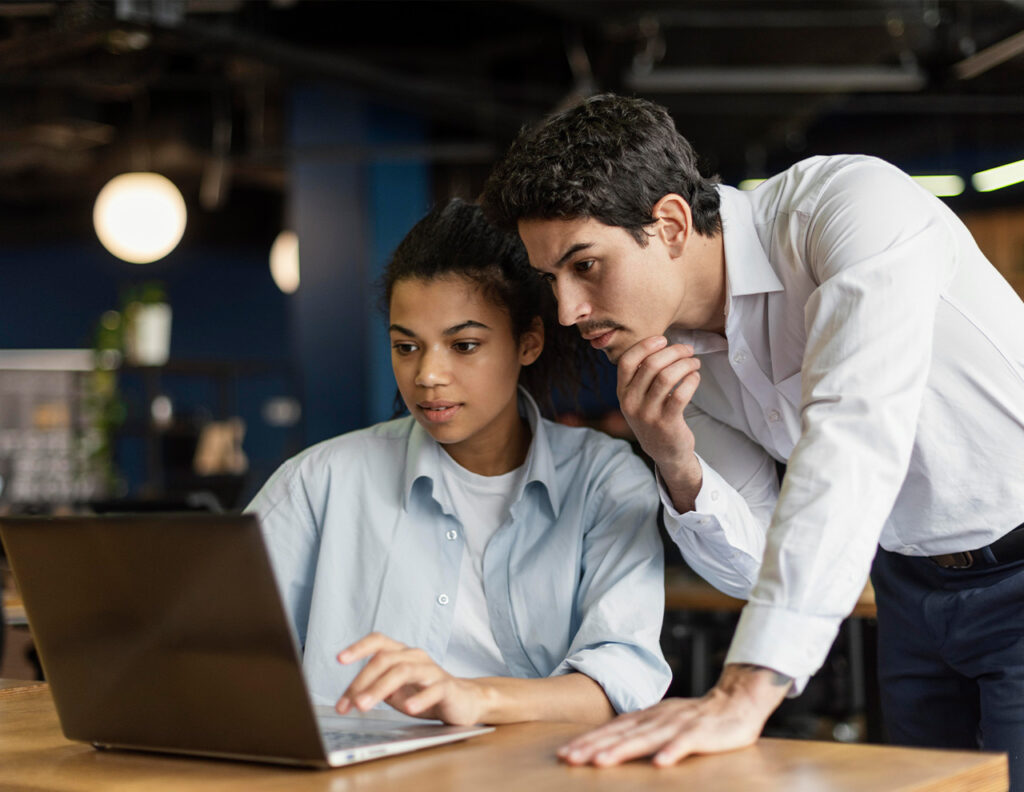 Hombre y mujer observan una computadora portátil en un entorno de oficina con colores oscuros y luces suaves.