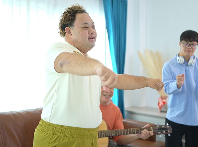 Hombre gesticulando mientras canta, acompañado de otro con guitarra en un entorno iluminado y acogedor.
