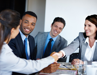 Cuatro personas en un entorno de oficina se reúnen, dos hombres y dos mujeres, mientras una mujer estrecha la mano de un hombre. Predominan tonos grises y azules.