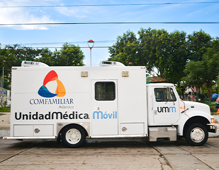 Camión de unidad médica móvil con el logo de Comfamiliar Atlántico, estacionado en un entorno urbano con árboles y un cielo parcialmente nublado.