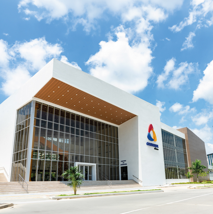 Edificio moderno con fachada de vidrio y detalles en madera, rodeado de cielo azul y nubes.