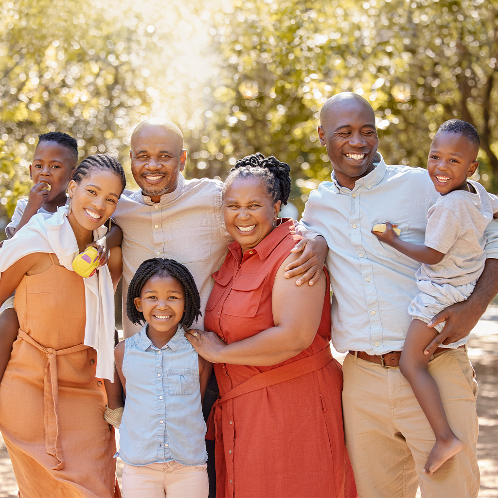Grupo familiar sonriente en un entorno natural, con seis personas de diferentes edades. Predominan colores cálidos y alegres, destacando vestimentas en tonos naranja y azul claro.
