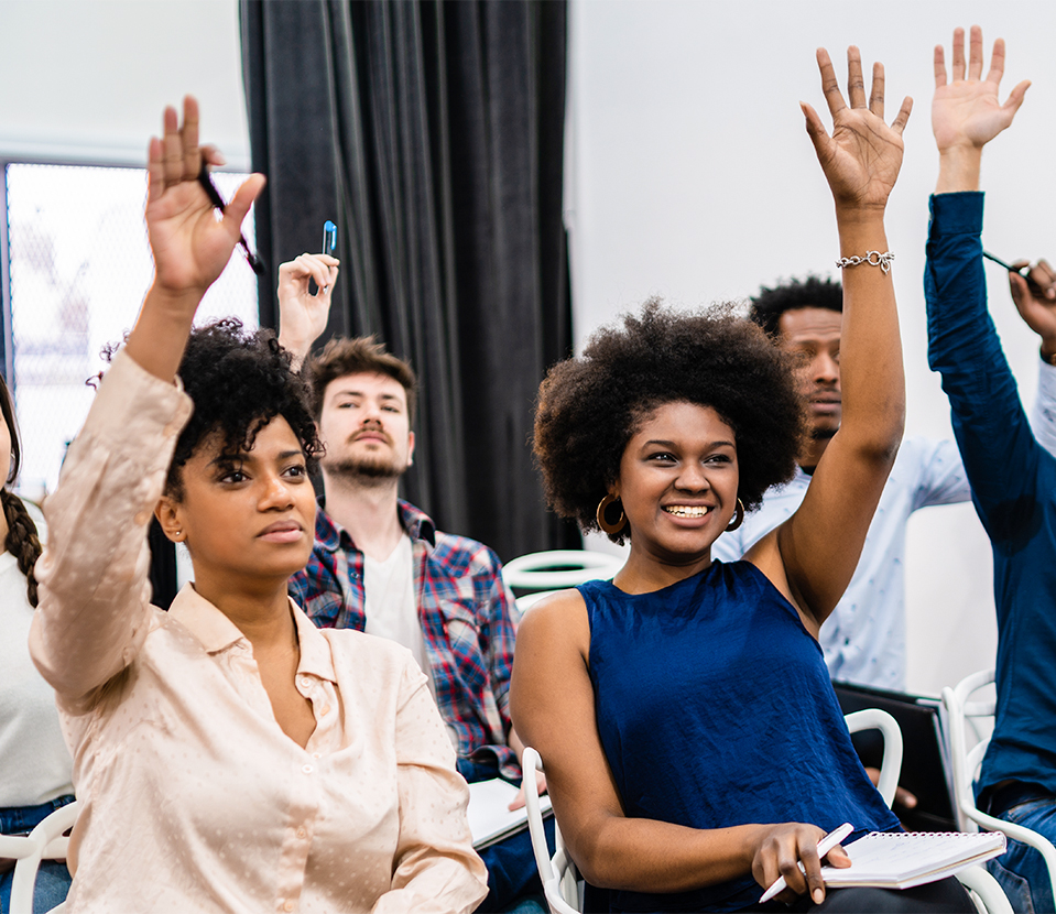 Grupo de personas levantando la mano en un entorno de aula, con diversos estilos de cabello y vestimenta.